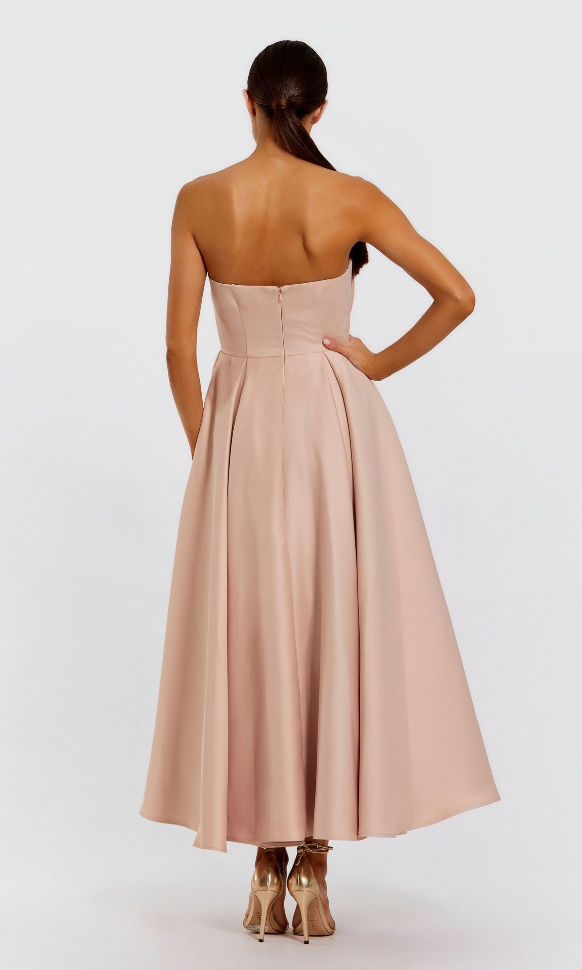 A woman stands with her back to the camera, wearing the Mac Duggal 2330 Emerald Tea-Length Formal Dress and high heels against a plain background.